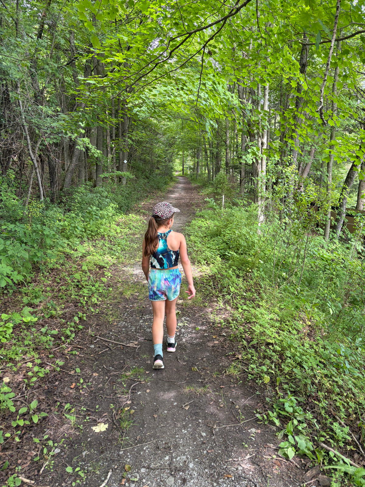 A young girl walking away on a dirt path through Durham Forest in Uxbridge, a lush green forest. Enjoying Forest Fridays with Woodland Skin Renewal.