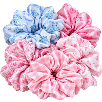 Five Silk hair scrunchies arranged together on a white background, featuring different patterns: blue floral print, pink cherry print, pink gingham, and pink floral print.