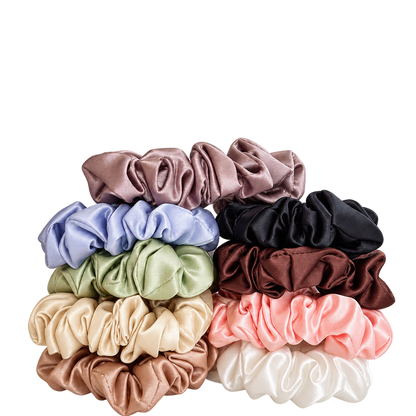 A stack of eight silk hair scrunchies in assorted colours, including mauve, light blue, black, olive green, burgundy, beige, pink, and white, arranged on a plain white background.